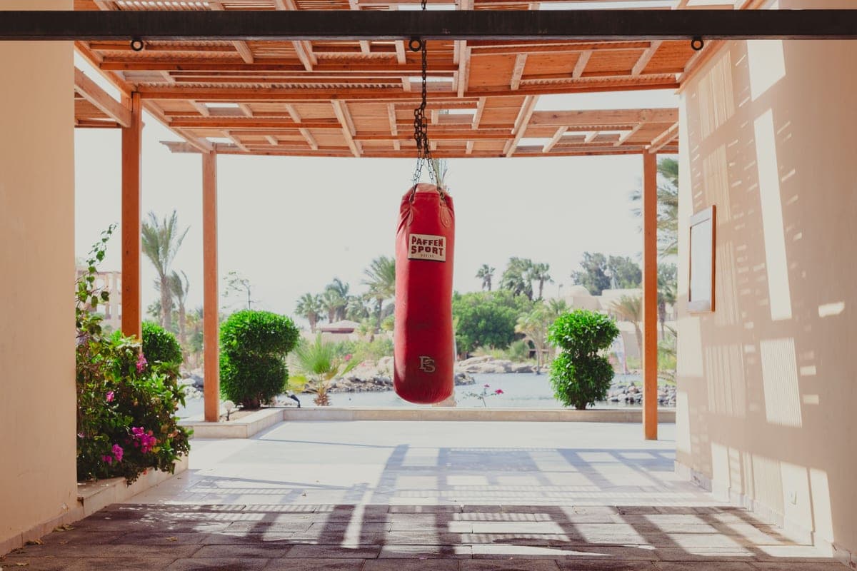 A red punching bag hanging in a sunny training space