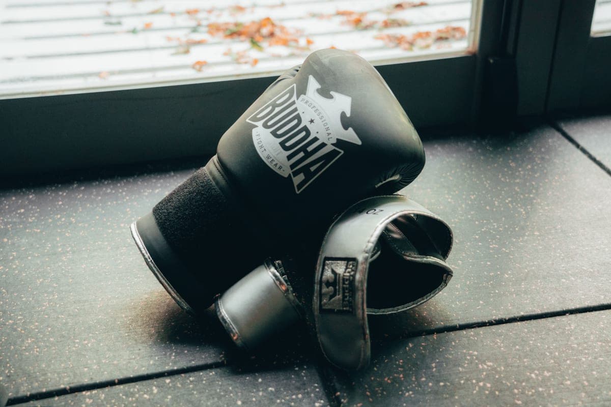 A pair of black boxing gloves on a gym floor near a window