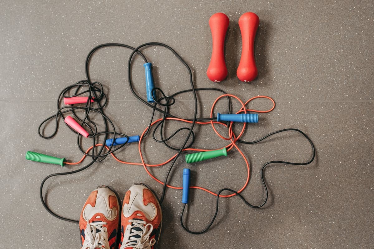 Jump ropes, dumbbells and training shoes laid out on a gym floor