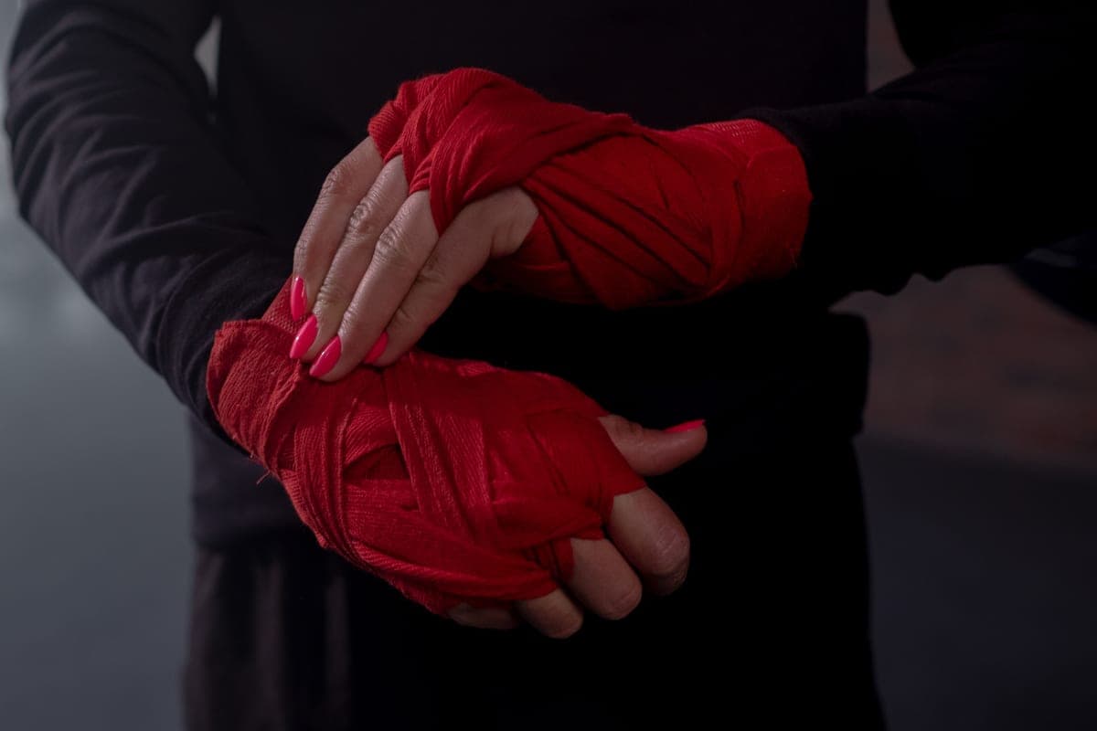 A person wrapping their hands with red boxing hand wraps